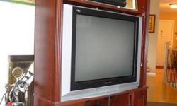 Corner TV Unit
Cherry colour, includes Panasonic TV (if you want it).
36" wide, 57" high, 19" deep.  Will hold a TV 32" maximum.
Two cupboards on bottom for DVDs or tapes.
Two shelves behind glass doors at bottom for PVR, DVD player etc.
One adjustable